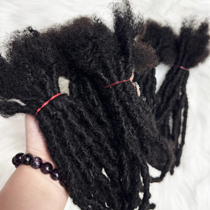Black braided hair extensions held by a hand with a bracelet on a white background
