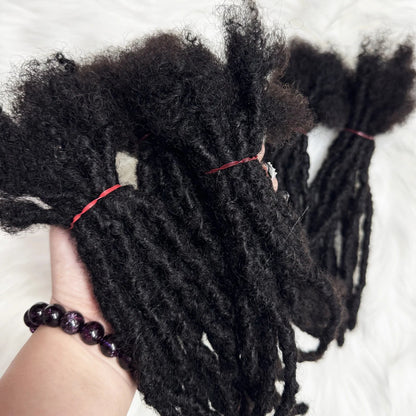 Black braided hair extensions held by a hand with a bracelet on a white background